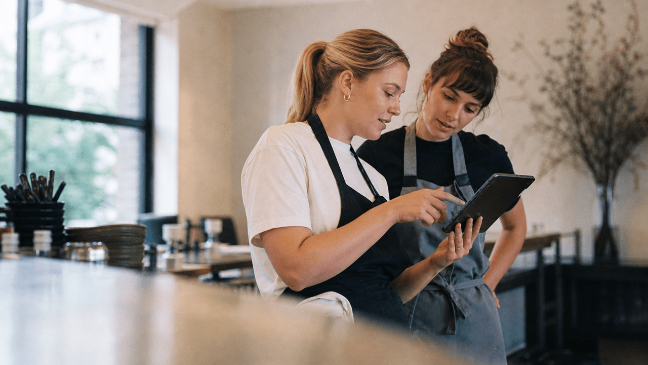 Twee restaurantmedewerkers die voor opening voorraadsoftware doorlopen op een tablet bij de servicebalie