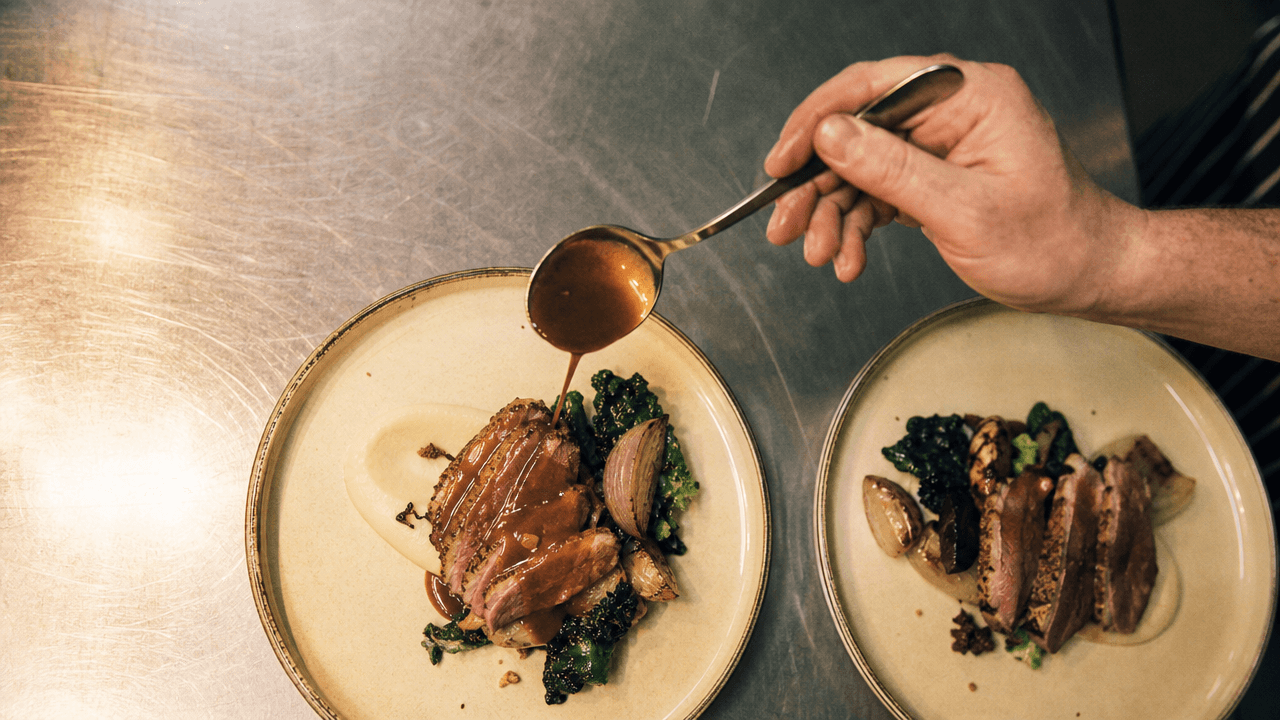 Kok die twee opgemaakte gerechten afmaakt met een schep saus, het gelijkmatig opmaken dat de foodcostafwijking laag houdt